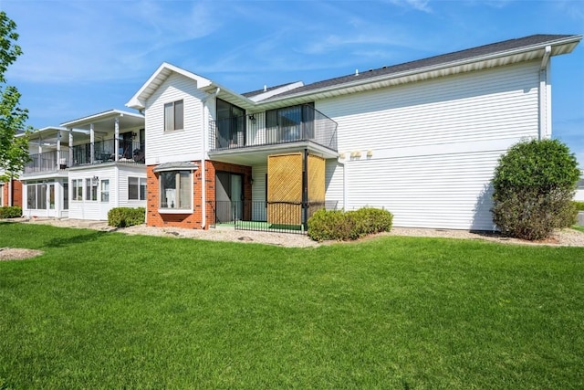 rear view of house with brick siding, a yard, and a balcony