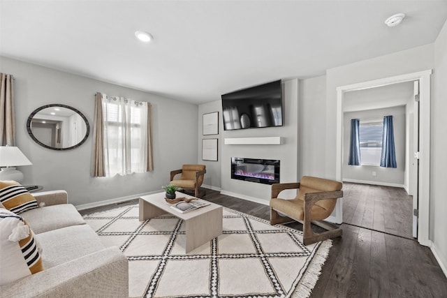 living room with a glass covered fireplace, baseboards, wood-type flooring, and visible vents