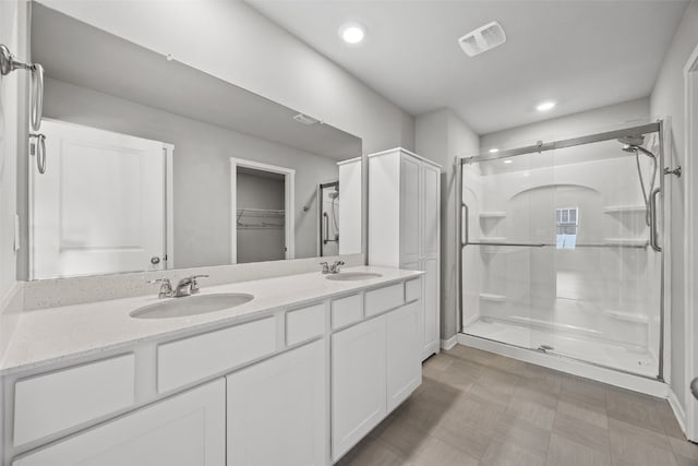 bathroom with a sink, a shower stall, double vanity, and visible vents