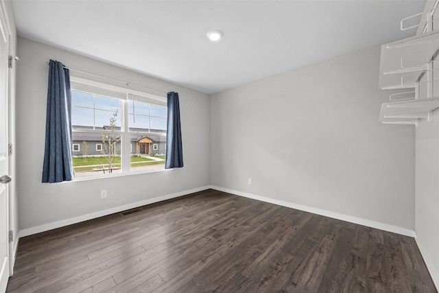 spare room with baseboards, dark wood-style floors, and visible vents