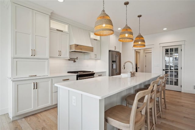 kitchen with a sink, custom exhaust hood, light wood finished floors, stainless steel appliances, and recessed lighting