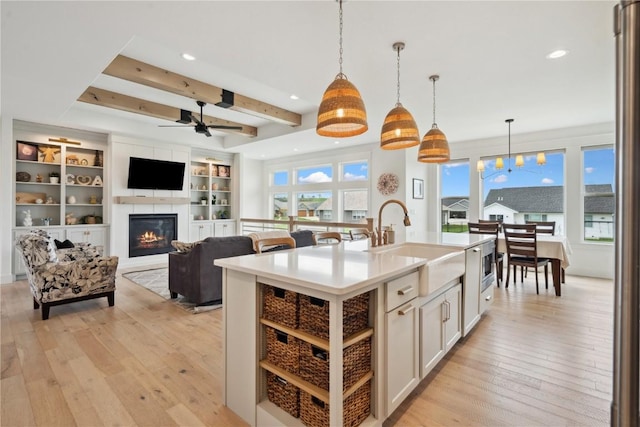 kitchen with light wood-type flooring, a sink, a glass covered fireplace, and ceiling fan