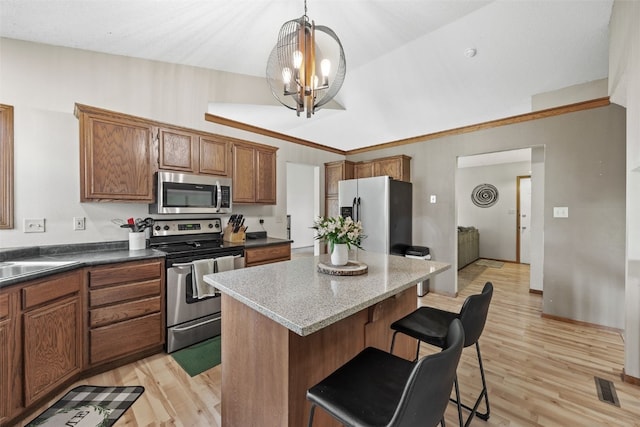 kitchen with a kitchen bar, a center island, brown cabinets, a chandelier, and stainless steel appliances