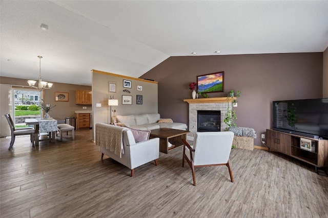 living area featuring an inviting chandelier, a glass covered fireplace, wood finished floors, and vaulted ceiling