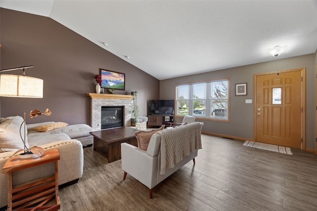 living area featuring a glass covered fireplace, baseboards, wood finished floors, and lofted ceiling