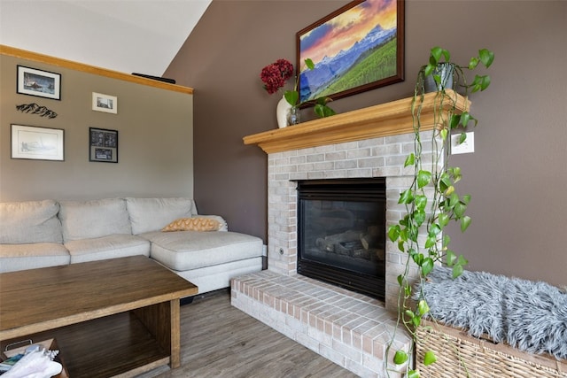 living area featuring a brick fireplace, vaulted ceiling, and wood finished floors