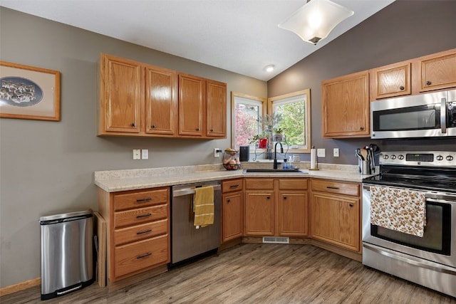 kitchen with light countertops, stainless steel appliances, vaulted ceiling, and a sink