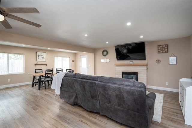 living area with a brick fireplace, baseboards, recessed lighting, light wood-type flooring, and a ceiling fan