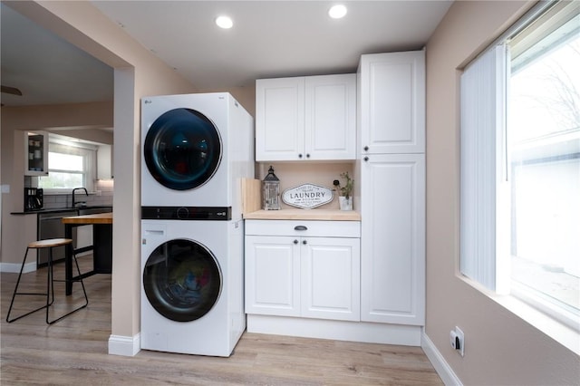 clothes washing area featuring light wood-style floors, stacked washer and clothes dryer, cabinet space, and recessed lighting