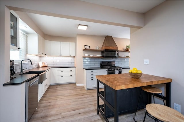 kitchen with white cabinets, a sink, light wood finished floors, stainless steel appliances, and backsplash
