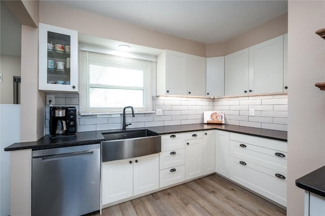 kitchen with dark countertops, a sink, dishwasher, white cabinetry, and light wood-type flooring