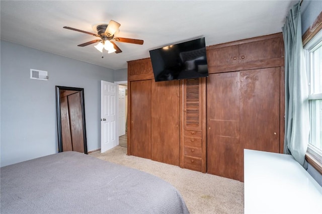 bedroom featuring visible vents, a ceiling fan, multiple windows, and light colored carpet