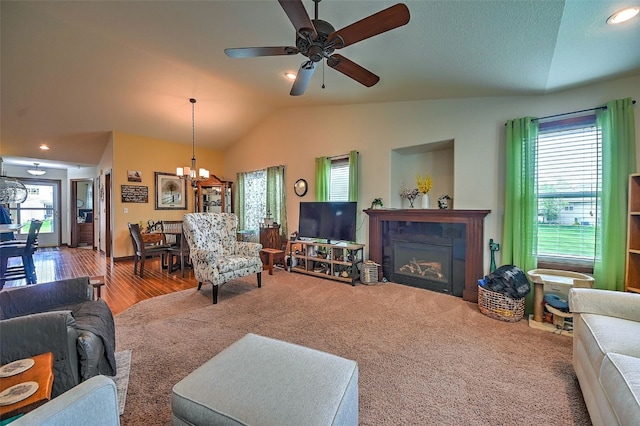 living room featuring vaulted ceiling, wood finished floors, ceiling fan with notable chandelier, a glass covered fireplace, and recessed lighting