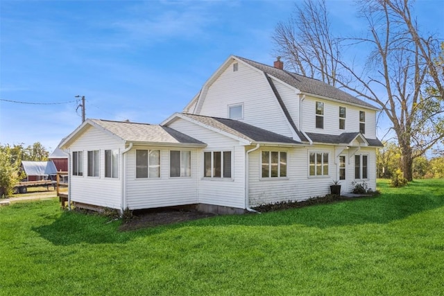 rear view of property featuring a lawn, a chimney, a gambrel roof, and roof with shingles