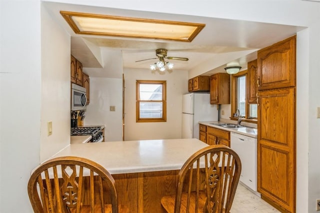kitchen featuring ceiling fan, brown cabinetry, a sink, light countertops, and white appliances