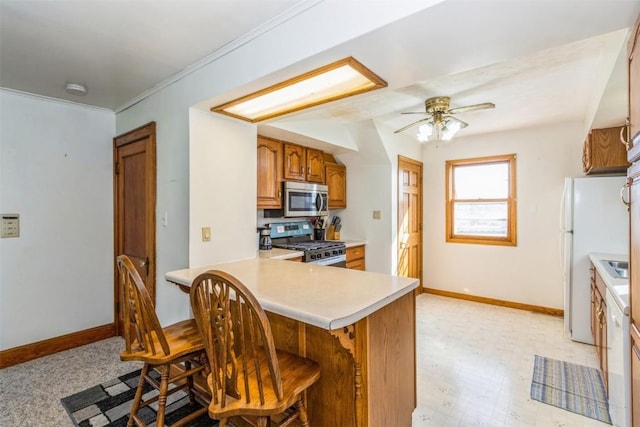 kitchen featuring a breakfast bar, baseboards, light countertops, brown cabinets, and appliances with stainless steel finishes