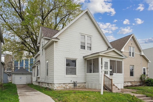 view of front of property featuring a front yard, roof with shingles, a sunroom, concrete driveway, and a detached garage
