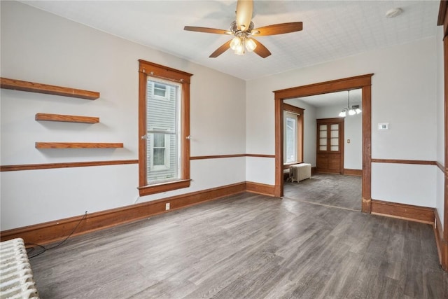 empty room with radiator heating unit, baseboards, ceiling fan, and wood finished floors