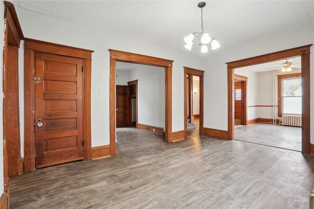 spare room with radiator, baseboards, ceiling fan with notable chandelier, and wood finished floors