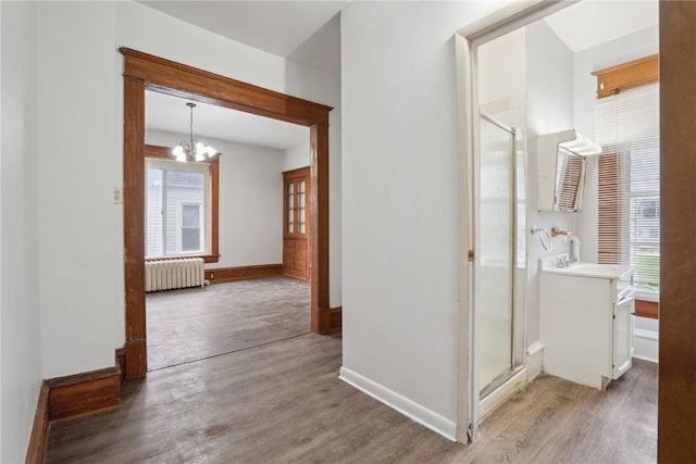 corridor with baseboards, an inviting chandelier, radiator heating unit, and wood finished floors