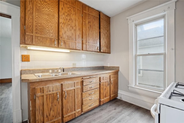 kitchen featuring baseboards, white range with gas cooktop, a sink, and light wood-style floors