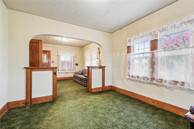 spare room featuring a healthy amount of sunlight, arched walkways, baseboards, and carpet floors