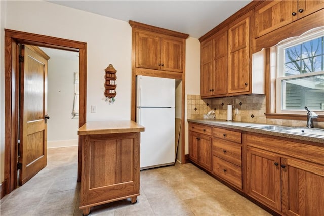 kitchen featuring tasteful backsplash, brown cabinets, a sink, baseboards, and freestanding refrigerator