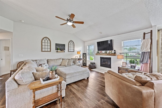 living room featuring a ceiling fan, a textured ceiling, dark wood finished floors, lofted ceiling, and a glass covered fireplace
