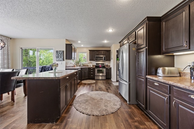 kitchen with stainless steel appliances, a textured ceiling, dark brown cabinetry, and dark wood-type flooring