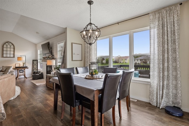 dining space featuring dark wood-style flooring, a glass covered fireplace, lofted ceiling, baseboards, and a chandelier