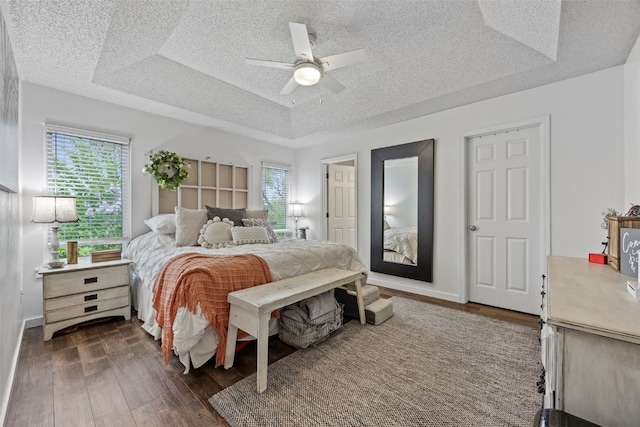 bedroom with ceiling fan, a tray ceiling, dark wood-style flooring, and a textured ceiling