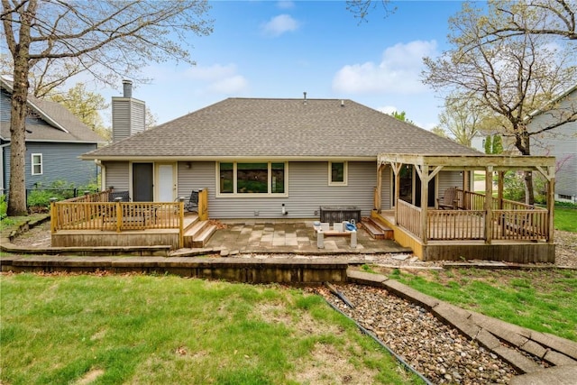 back of house with a wooden deck, a chimney, a shingled roof, a patio area, and a yard
