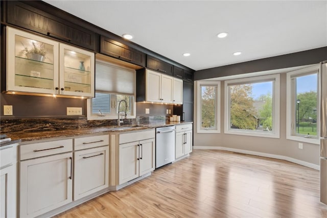 kitchen with dishwasher, a sink, baseboards, dark stone countertops, and light wood-style floors