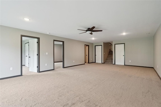 unfurnished room featuring baseboards, ceiling fan, light carpet, and stairway