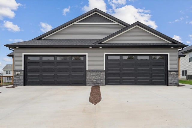 view of front of home featuring central AC, stone siding, a shingled roof, an attached garage, and driveway