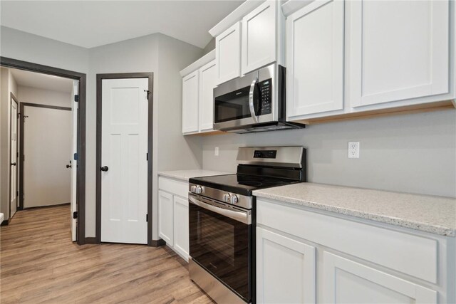 kitchen with appliances with stainless steel finishes, light stone counters, light wood-type flooring, and white cabinetry
