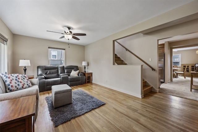 living area with stairs, ceiling fan, wood finished floors, and a healthy amount of sunlight