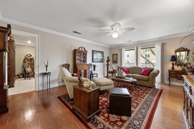 living room with a ceiling fan, visible vents, crown molding, wood finished floors, and baseboards