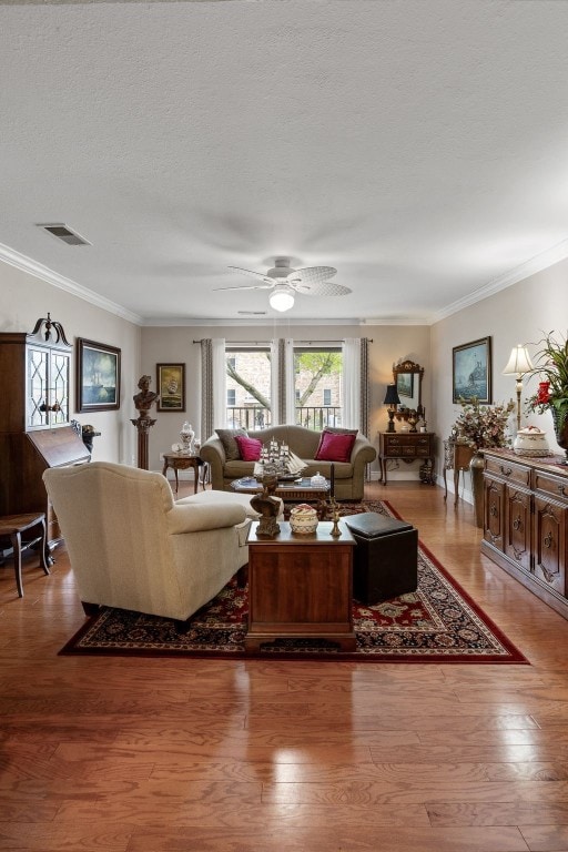 living area with crown molding, ceiling fan, a textured ceiling, wood finished floors, and visible vents