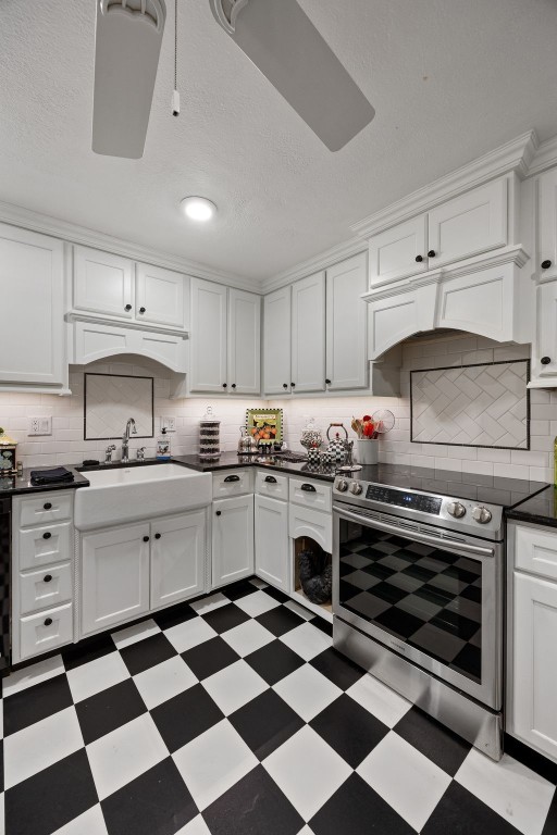 kitchen featuring dark countertops, a sink, stainless steel range with electric stovetop, tile patterned floors, and white cabinetry