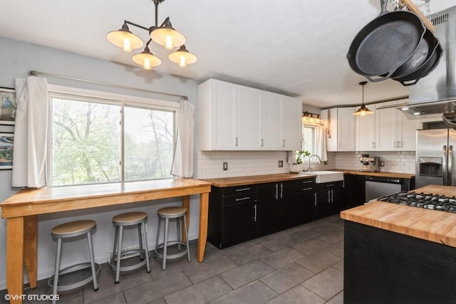 kitchen featuring wooden counters, white cabinets, dark cabinetry, a sink, and stainless steel appliances