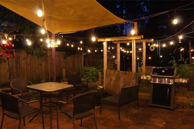 patio at twilight with outdoor dining area, fence, and area for grilling