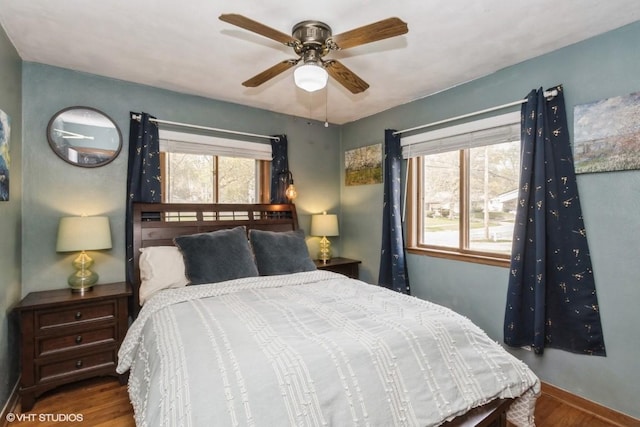 bedroom featuring baseboards, ceiling fan, multiple windows, and wood finished floors