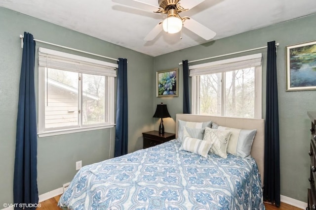bedroom with baseboards, ceiling fan, wood finished floors, and multiple windows