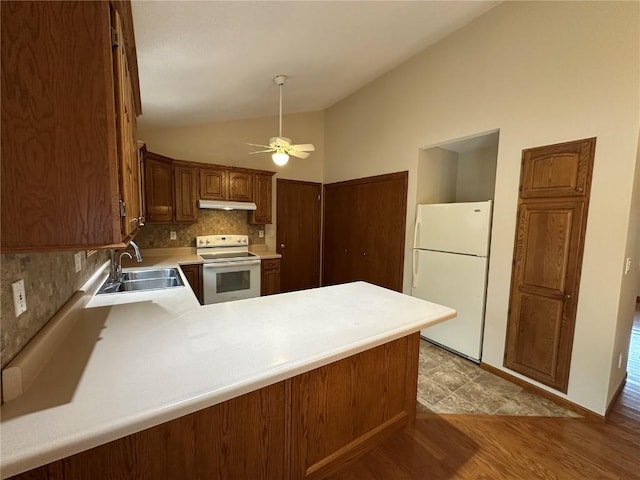 kitchen with a peninsula, white appliances, under cabinet range hood, a sink, and vaulted ceiling