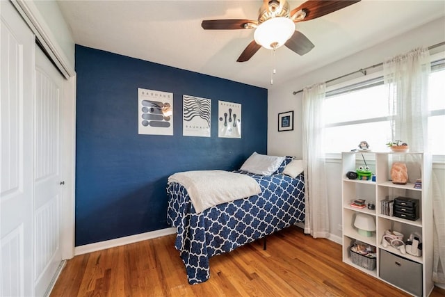 bedroom with a ceiling fan, baseboards, wood finished floors, and a closet