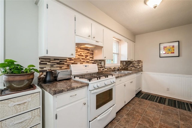 kitchen featuring white appliances, white cabinets, under cabinet range hood, and dark countertops