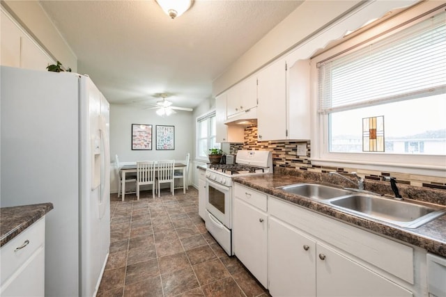 kitchen featuring a ceiling fan, dark countertops, a sink, white cabinets, and white appliances
