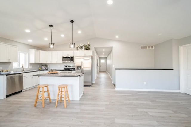 kitchen featuring light wood finished floors, a center island, stainless steel appliances, vaulted ceiling, and visible vents