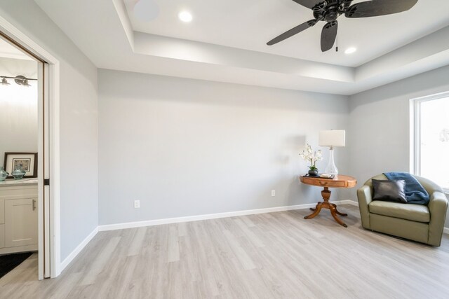sitting room with light wood-style floors, baseboards, ceiling fan, and a raised ceiling